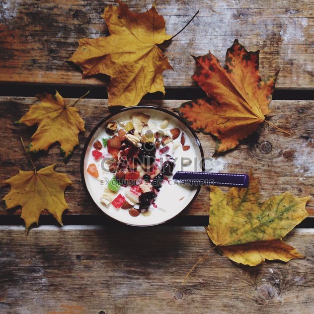 Muesli with dried fruit and nuts for breakfast and yellow leaves on wooden background - Kostenloses image #198377