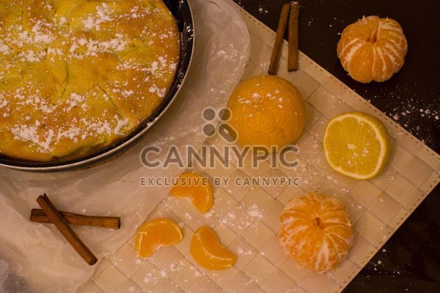 Charlotte with cinnamon and tangerines on table - бесплатный image #182597