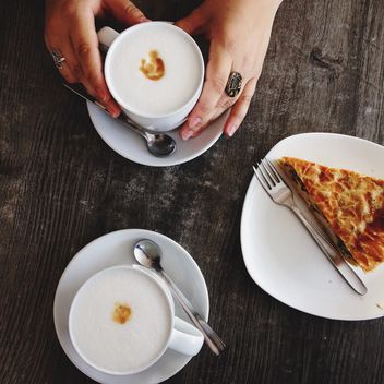 Cup of coffee in female hands and piece of pie on wooden background - бесплатный image #198397